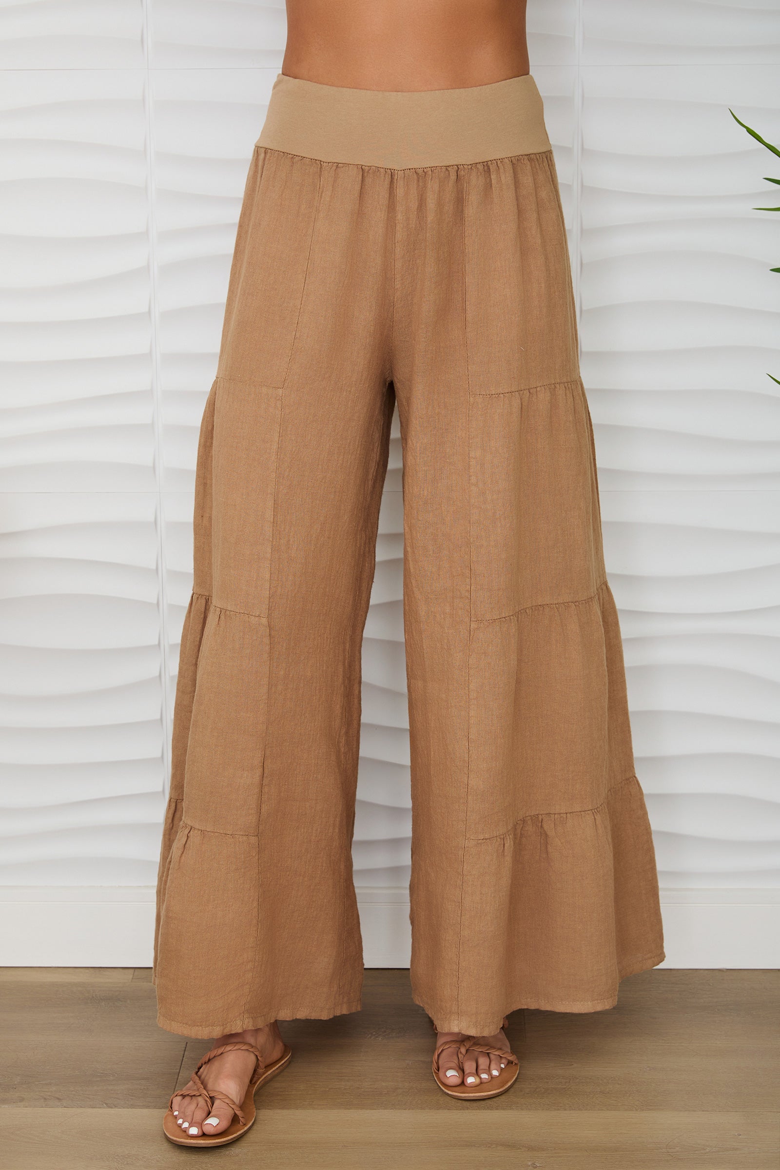 Brown wide-leg pants worn by a person against a white textured wall.